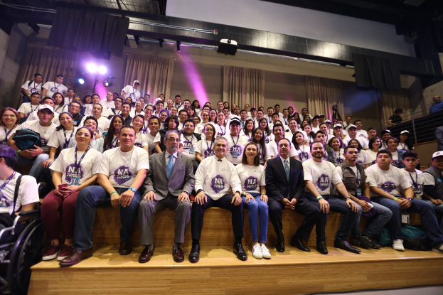 Gruppe von Menschen auf einer Bühne mit einer Person im Rollstuhl links, Vorhänge und Beleuchtung im Hintergrund bei einer NBA-Frauenbasketball-Konferenz