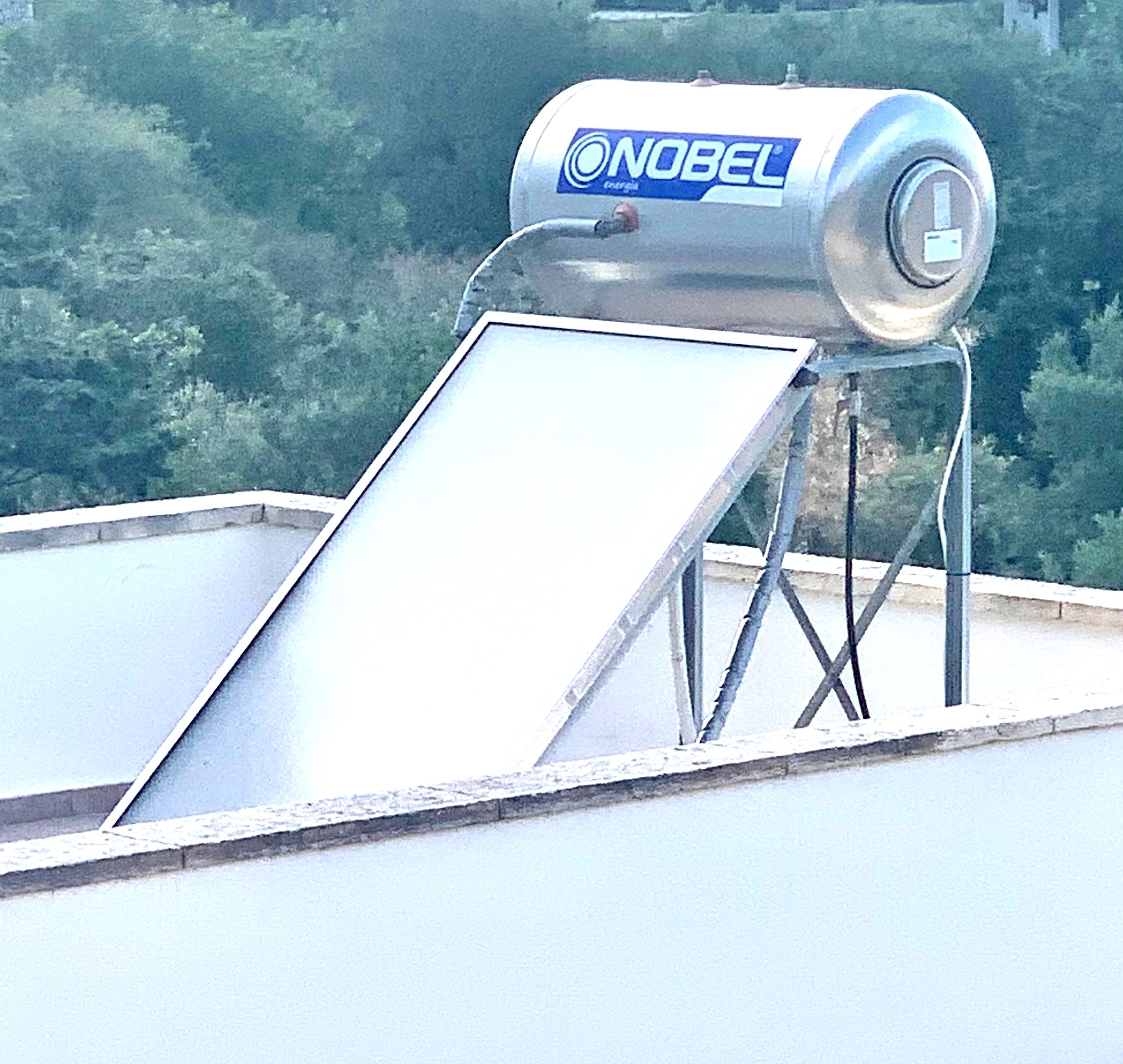 Solar-Wassererwärmer mit Speicher auf einem Gebäudedach, Bäume im Hintergrund.