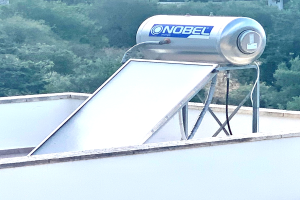 Solar-Wassererwärmer mit Speicher auf einem Gebäudedach, Bäume im Hintergrund.