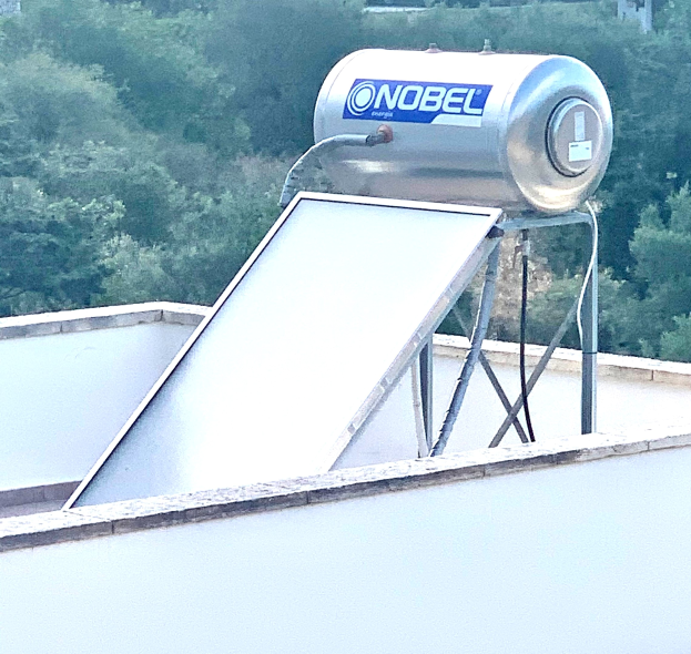 Solar-Wassererwärmer mit Speicher auf einem Gebäudedach, Bäume im Hintergrund.