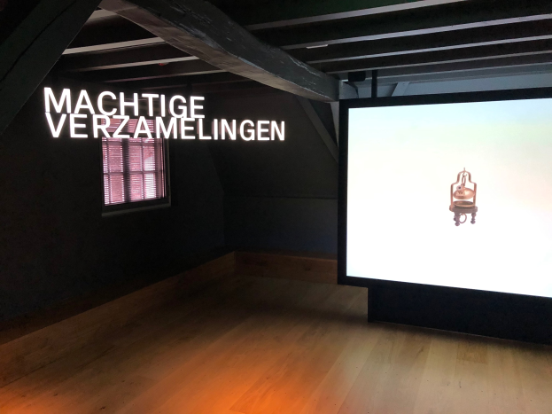 Ausstellungsansicht mit dem Titel 'Machtige Verzamelingen' im Museum of Modern Art in Berlin, mit einem großen Bildschirm auf der rechten Seite und einem Fenster auf der linken Seite.