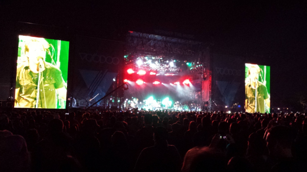 Ein Konzertszene mit einer Menge unten, einem großen Bildschirm links und einem kleineren Bildschirm rechts.