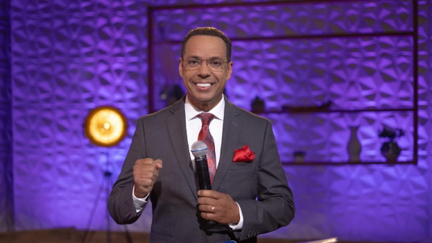 Stephen Colbert, Moderator von "The Daily Show with Trevor Noah", steht auf einer Bühne und hält ein Mikrofon, trägt einen Anzug, Krawatte und eine Brille, mit einem Scheinwerfer und Ständer im Hintergrund.