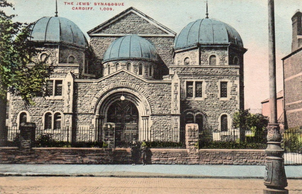 Eine alte Ansichtskarte zeigt die jüdische Synagoge in Cardiff, Ontario, Kanada, mit einem Gebäude mit Fenstern, Türen und Bögen, umgeben von Pflanzen, einem Zaun, einer Gruppe von Bäumen, einem Pfahl und einem bewölkten Himmel, mit Text oben.