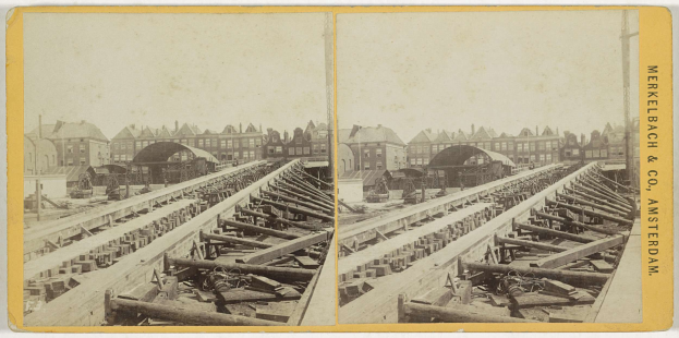 Schwarz-weiß-Foto einer Bahntrasse mit Gebäuden im Hintergrund, Text 'Merkelbach & Co, Co. Amsterdam' rechts und hälftierte Gegenstände im Vordergrund.