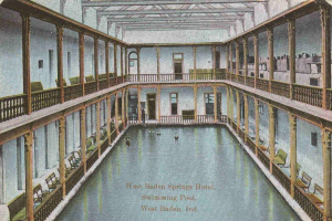 Alte Postkarte des großen Hallen-Schwimmbads im West Baden Springs Hotel mit Menschen, Säulen, Geländern, Stühlen und Text unten.