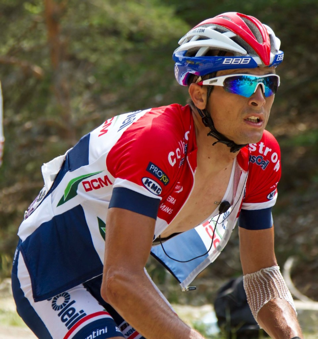 Ein Mann mit Schutzbrille und Helm steht vor einer Gruppe von Bäumen.