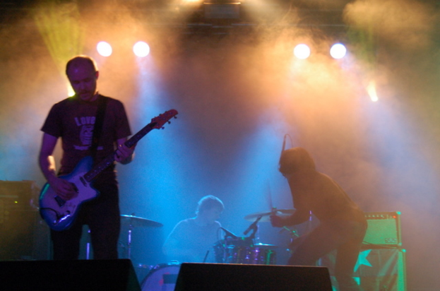 Ein musikalisches Konzert mit Lichtern oben, Musikern, die Instrumente in der Mitte spielen, und Lautsprechern auf beiden Seiten.