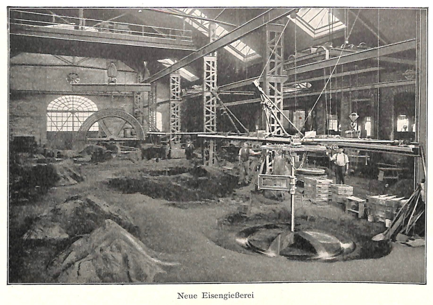Schwarzes und weißes Foto einer Fabrik mit Arbeitern, die an Maschinen arbeiten, Metallstangen und -rohre, beschriftet mit "Neue Eisengießerei, die erste Fabrik Deutschlands" unten.