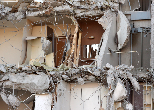 Ein teilweise abgetragenes Gebäude mit zerbrochenen Wänden und verstreuten Trümmern, darunter Holzstücke, in einem Zustand des Verfalls.