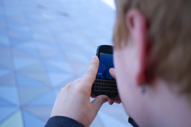 Eine Person hält ein Mobiltelefon in der Hand und steht auf einer Straße.