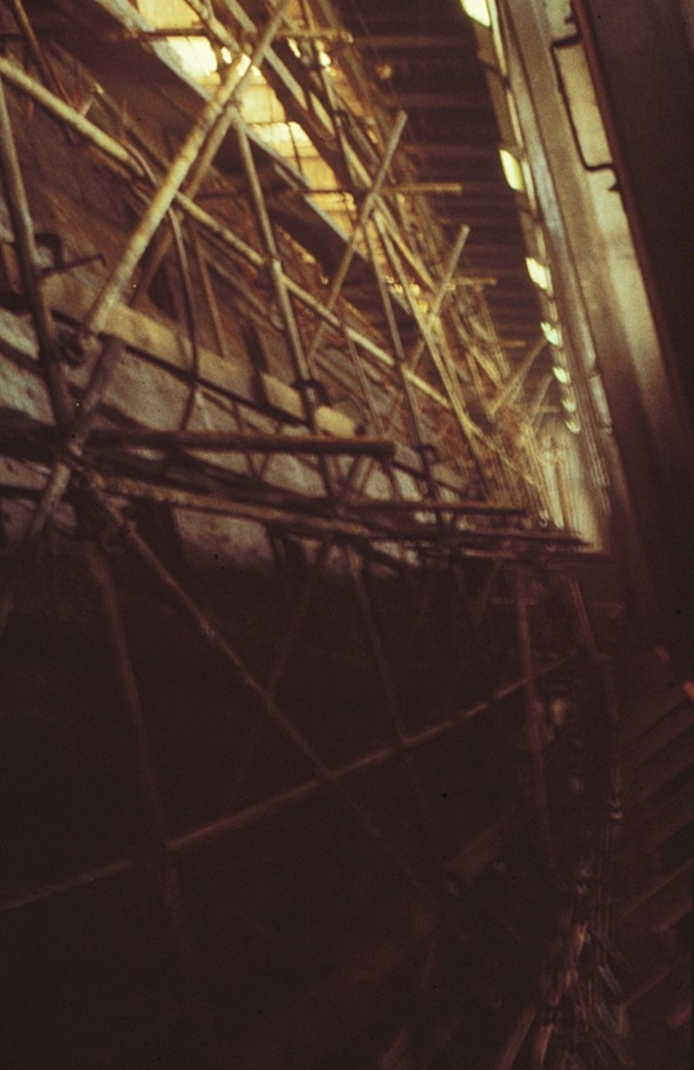 Ein Gebäude im Bau mit ausgedehntem Gerüst an der Seite, beleuchtet von Lichtern oben.