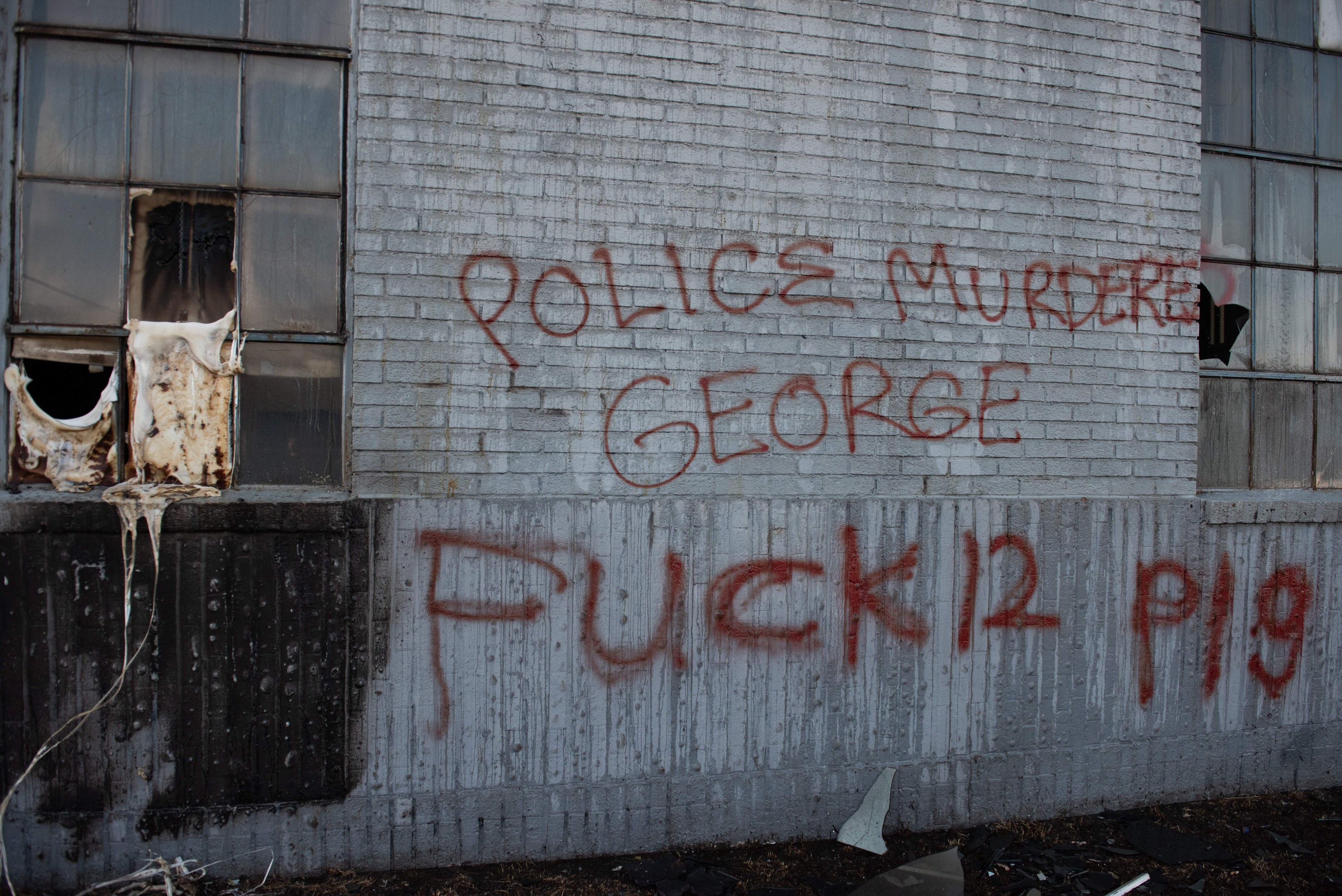 Schmiererei an einer Hauswand mit der Aufschrift "Polizeimord George Fuck 12 P19" mit Fenstern und verstreuten Gegenständen davor.