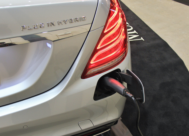 Ein weißes Elektroauto ist in eine Ladeeinrichtung an einem schwarzen Teppichboden eingesteckt, mit sichtbarem Text auf dem Auto.