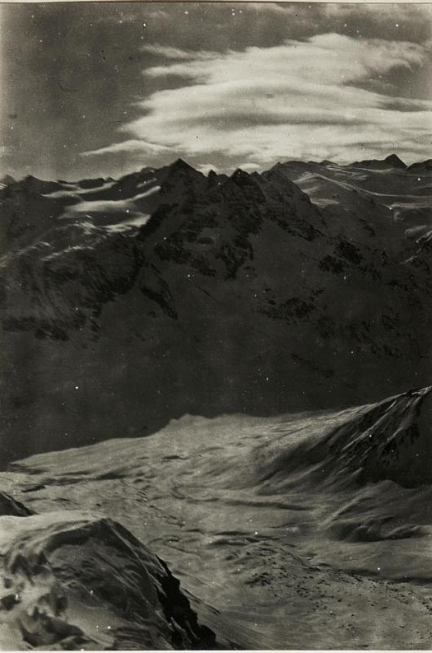 Ein Schwarz-Weiß-Foto einer Berglandschaft mit schneebedeckten Gipfeln und einer wolkenverhangenen Himmel, mit Text unten, der 'Gustav Klimt - The Alps' lautet.