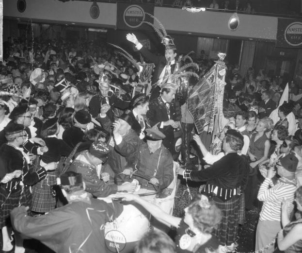 Ein Schwarz-Weiß-Bild einer Menge von Menschen in Schottenröcken, die auf einer Party tanzen, wobei einige Musikinstrumente und Schilder halten.