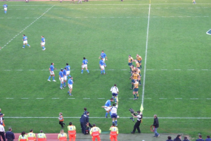 Einige Menschen auf einem Fußballplatz, einer hält eine Videokamera.