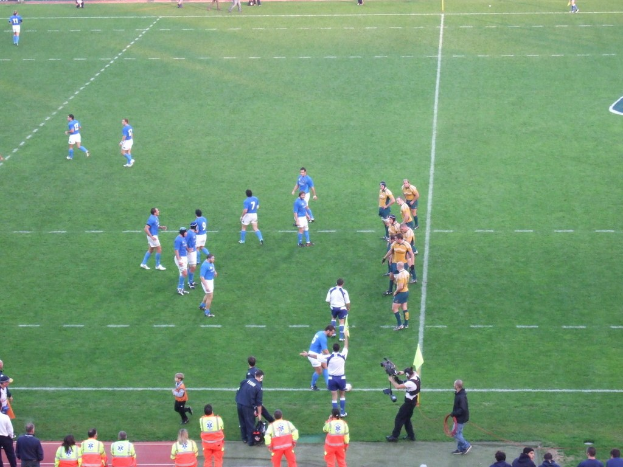 Einige Menschen auf einem Fußballplatz, einer hält eine Videokamera.