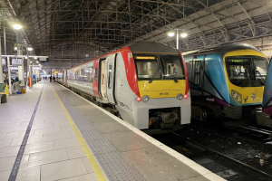 Zwei Züge nebeneinander auf einem Bahnhof geparkt mit einer Plattform auf der linken Seite, einige Menschen auf der Plattform und Straßenlaternen, die die Gegend beleuchten.