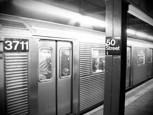 Ein Zug voller Menschen, mit einer Säule auf der rechten Seite, die ein Schild trägt, einer Plattform unten und einem Dach oben.