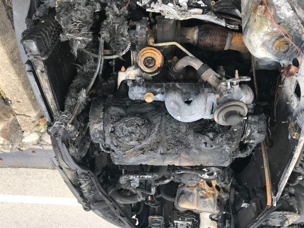 Ein verbrannter Automotor, verkohlt und schwarz, steht auf der Seite einer Straße neben einer Wand.