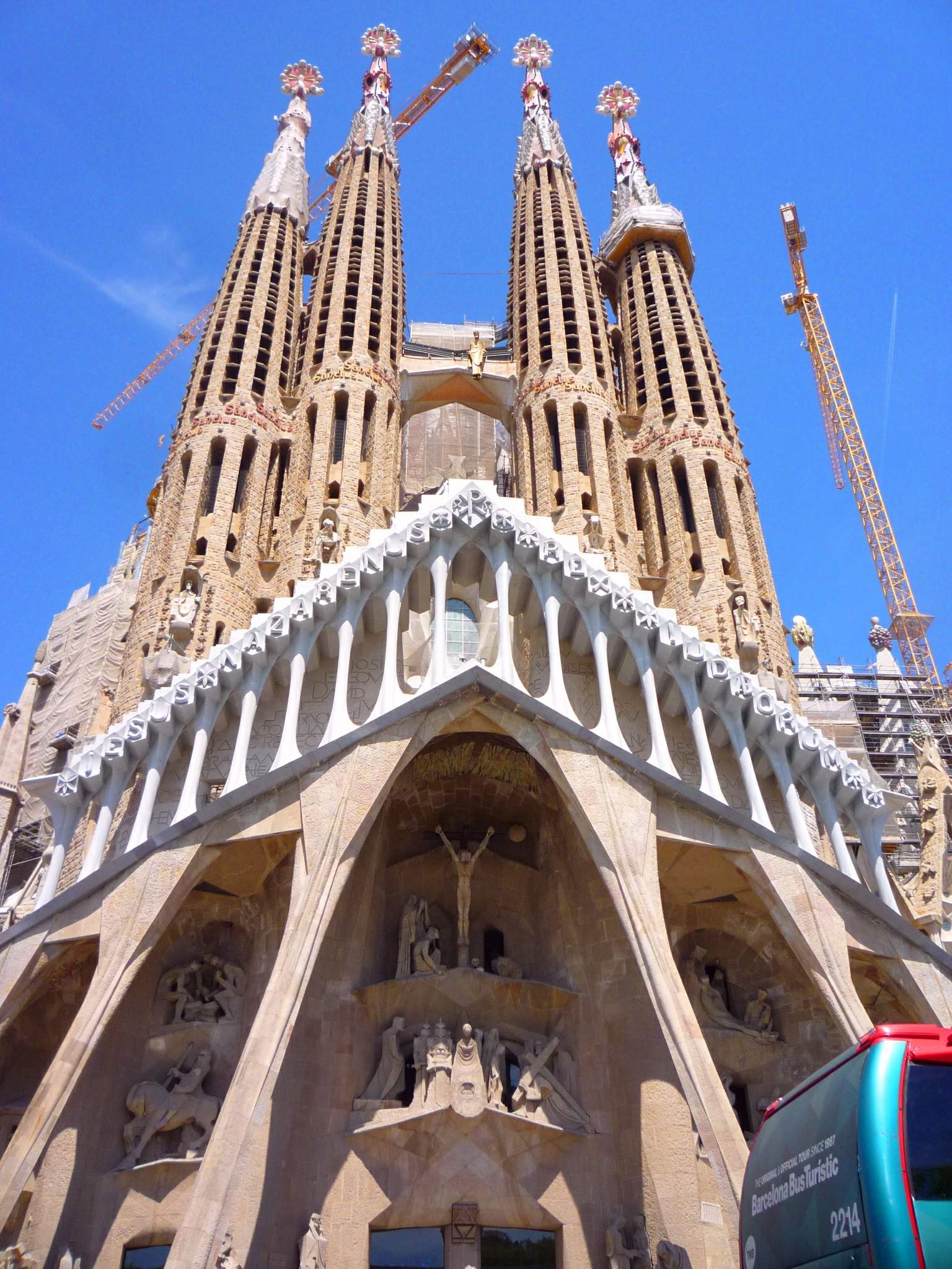 Die Sagrada Familia in Barcelona, Spanien, ein großes Gebäude mit detaillierten Skulpturen an seinen Wänden und Säulen, mit einem Fahrzeug davor und dem Himmel im Hintergrund.