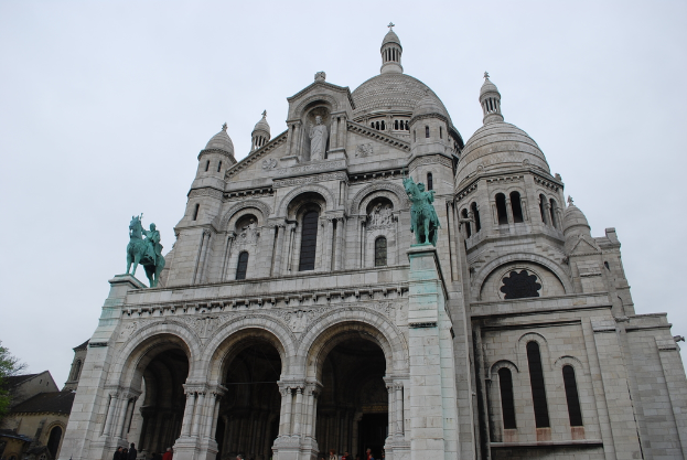 Ein Denkmal steht in der Mitte des Bildes, mit Häusern und einem Baum in der linken unteren Ecke.