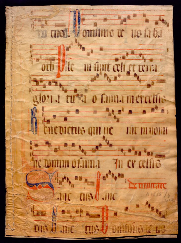 Ein illuminiertes Manuskript mit Musiknotation auf einem Blatt Papier vor einem dunklen Hintergrund, gefüllt mit Text und Musiksymbolen, die ein komplexes Design bilden.