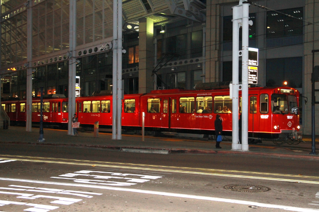Eine Gruppe von Menschen sitzt in einem roten Zug, mit Pfählen, Schildern und Lichtern draußen