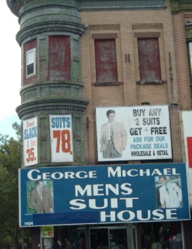 Ein Gebäude mit Plakaten an der Fassade, Stände unten, umgeben von Bäumen und Himmel.