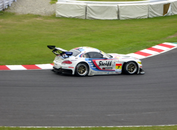 Ein Porsche 911 GT3 RSR fährt auf einer Rennstrecke mit grünem Gras und einem Zaun auf der linken Seite, verziert mit Text und Zahlen für die 24 Stunden von Le Mans.