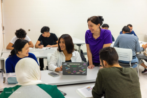 Eine Gruppe von Menschen, die um einen unordentlichen Tisch in einem Klassenzimmer sitzen und über Klimawandel diskutieren.