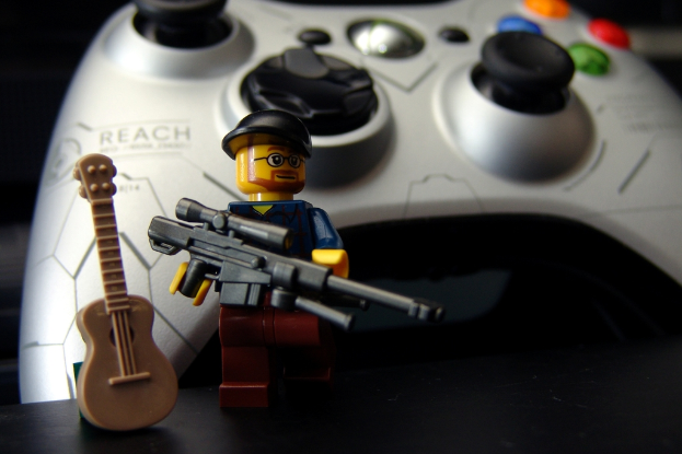 Eine Actionfigur mit einer Mütze tragend und eine Pistole haltend, mit einer Spielzeuggitarre daneben und einem Joystick mit Knöpfen im Hintergrund.
