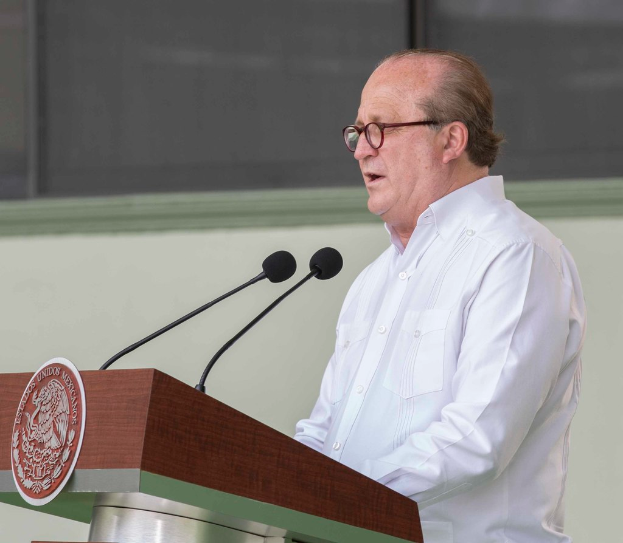 Ein Mann in einem weißen Hemd und Brille steht neben einem Rednerpult und spricht.