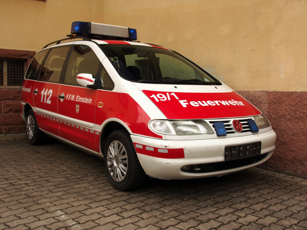 Rote und weiße Ambulanz mit Text und Zahlen vor einem Gebäude mit Fenstern geparkt.