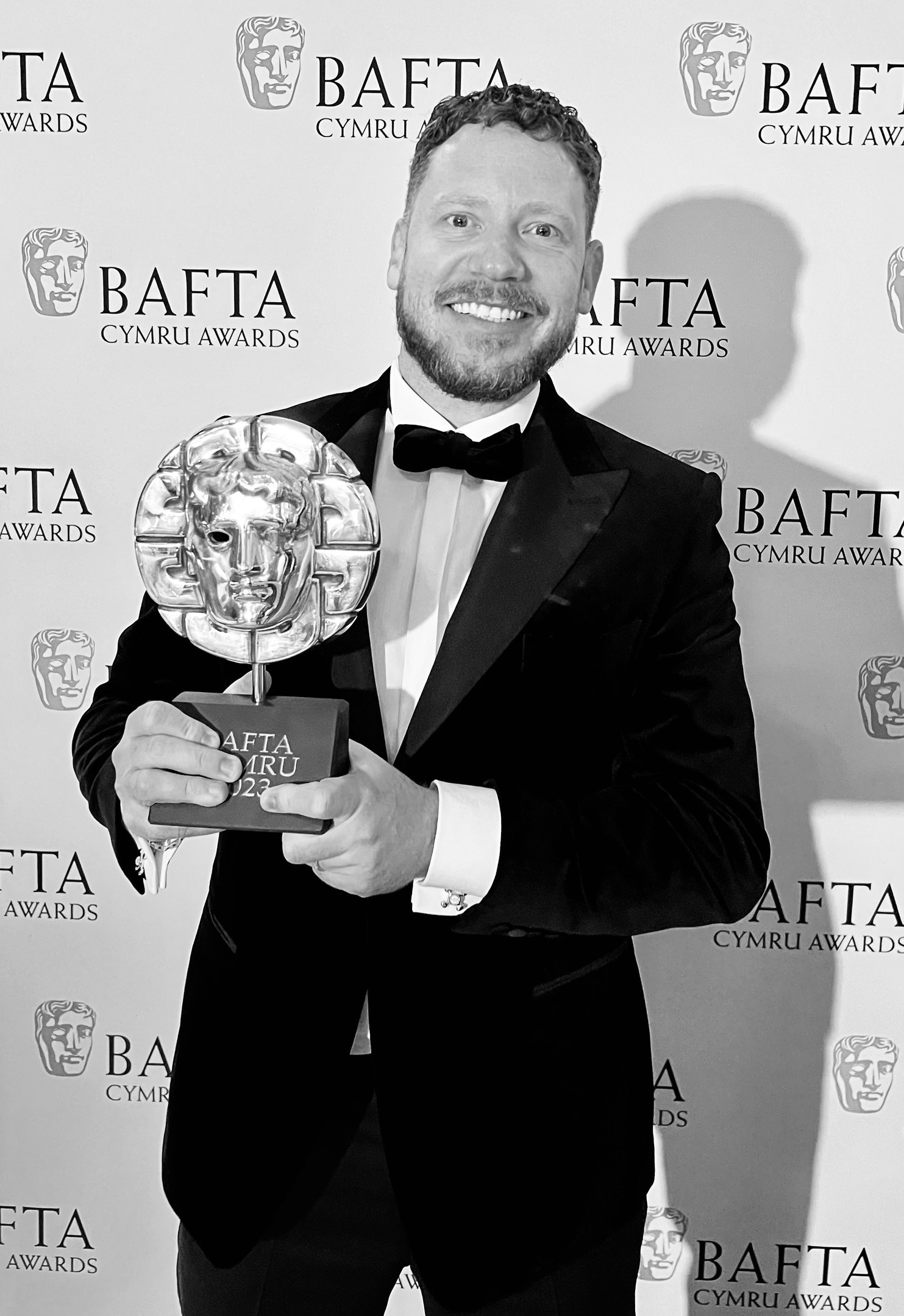 Ein Mann im Smoking, der eine BAFTA-Trophäe hält und lächelt, mit einem Hintergrundschild, auf dem "BAFTA Awards 2018" steht.