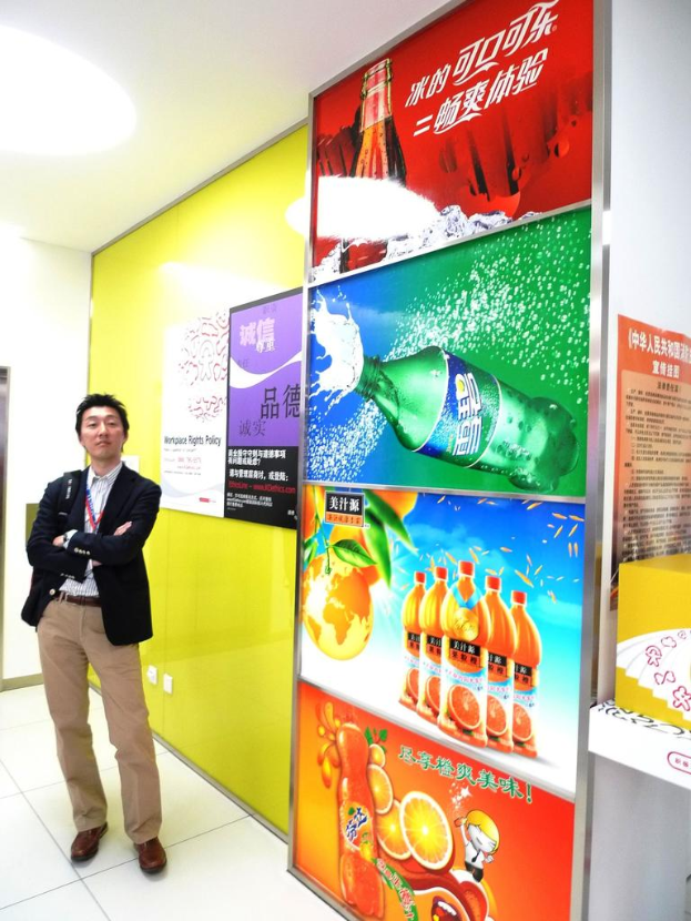 Ein Mann in einem Blazer steht vor einer Wand mit Softdrink-Werbung.