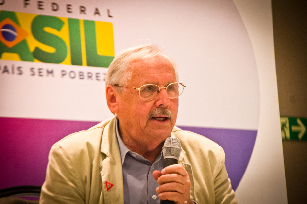 Eine Person, die in ein Mikrofon spricht und im Hintergrund ein Banner mit der Aufschrift 'Bundesstaat' sieht.