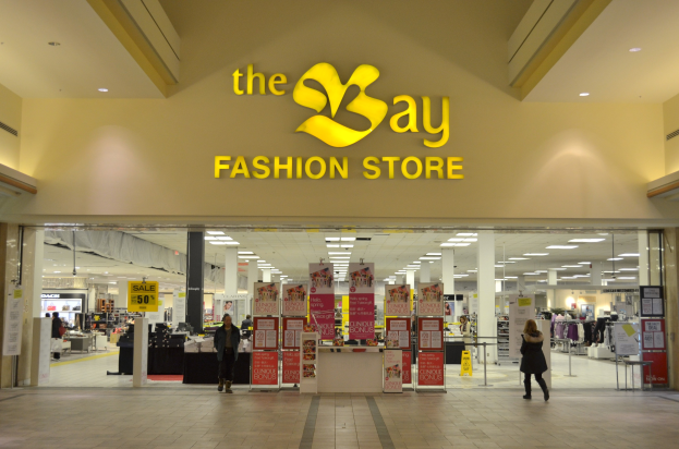 Ein Modegeschäft namens "bay" in einem Einkaufszentrum mit Einkäufern, Wandtextanzeigen, Säulen, Deckenleuchten und Hintergrunddekoration.