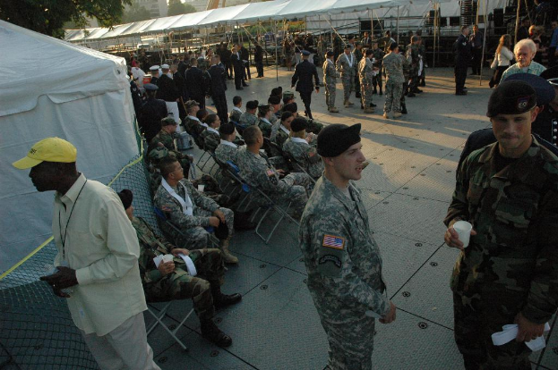 Eine Gruppe von Menschen in Militäruniformen versammelte sich draußen mit Zelten und einem Baum im Hintergrund, einige saßen auf Stühlen in der Mitte.