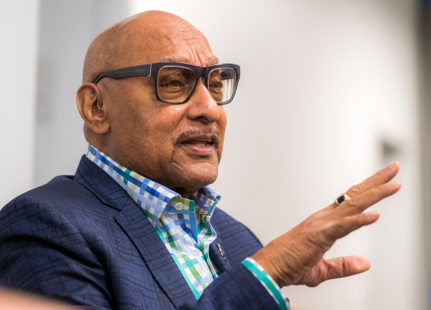 Ein Mann im Anzug und mit Brille spricht in ein Mikrofon und blickt auf ein Publikum mit unscharfem Hintergrund.