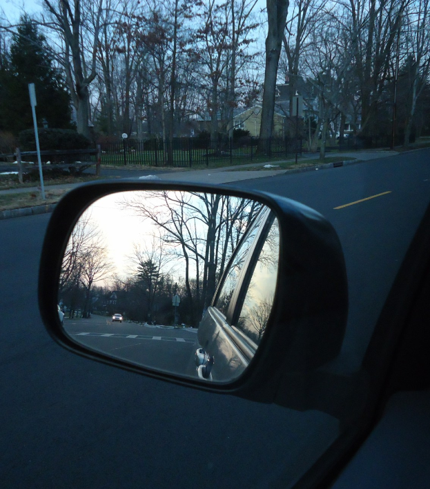 Eine Autos Seitenspiegelung auf der Straße, die Bäume, Gebäude und den Himmel reflektiert.