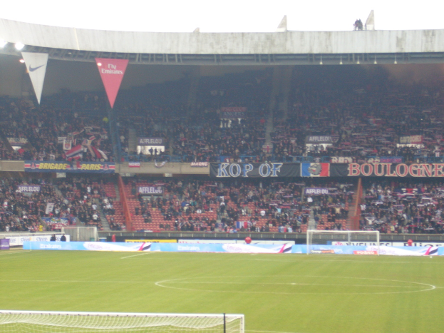 Ein Rasenboden mit Torpfosten auf beiden Seiten, Zuschauern im Hintergrund und zahlreichen Werbetafeln in der Mitte und oben.