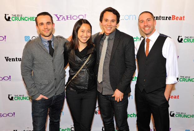 Eine Gruppe strahlender Menschen posiert mit einem Sponsorenbanner im Hintergrund.