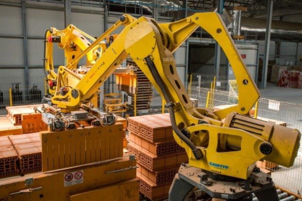 Großes industrielles Lagerhaus mit gestapelten Kisten, Überdachkränen, Zaun, Pfählen und einer fernen Wand in einer automatisierten Fertigungsumgebung.