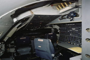 Das Cockpit eines Flugzeugs mit zwei Sitzen, einem Tisch mit einem Buch und verschiedenen elektronischen Geräten und Kabeln.