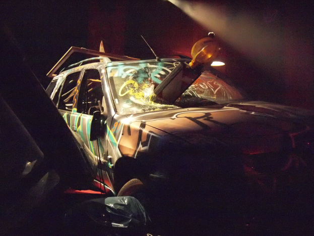 Ein verunglücktes Auto am Straßenrand in einem schlecht beleuchteten Gebiet, mit Rad und Reifen sichtbar.