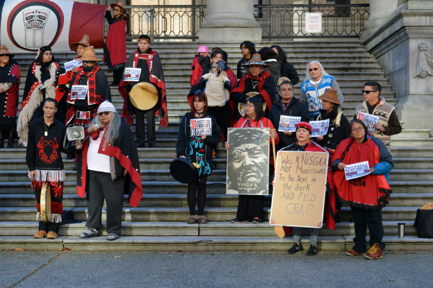Eine Gruppe von Menschen auf einer Treppe mit Plakaten und einem Lautsprecher, wobei eine Person ein Banner im Hintergrund hält.