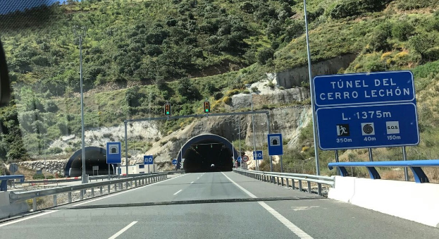 Auto fährt durch einen Tunnel mit Geländern, Schildern, Polen, Verkehrszeichen, Bäumen, Felsen und einem klaren blauen Himmel.