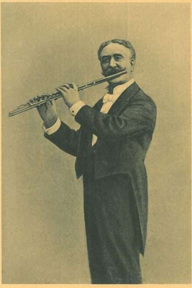 Ein altes Schwarz-Weiß-Foto eines Mannes in einem Smoking, der auf der Bühne eine Flöte spielt und die Augen geschlossen hat.